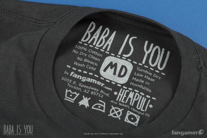 A photo of the screenprinted tag information on a Medium Baba Is Shirt t-shirt, featuring the Baba Is You, Fangamer, and Hempuli logos as well as care information (machine wash cold, no bleach, tumble dry low heat.)