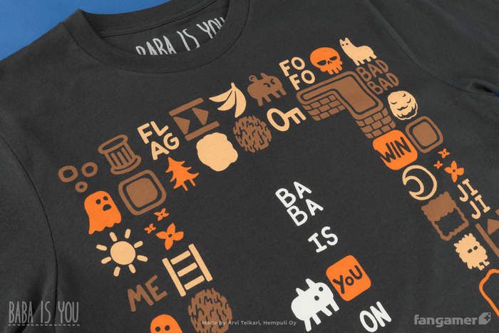 A closeup of the Baba Is Shirt t-shirt focusing on the top of the design; the frame of tiles surrounding Baba includes words like FLAG, ME, FOFO, and BADBAD as well as characters like a ghost and items like a key and ladder.