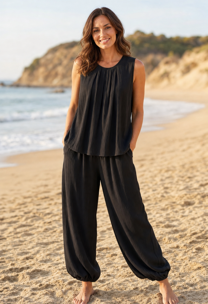 Woman wearing a black sleeveless top and wide-leg pants on a beach.