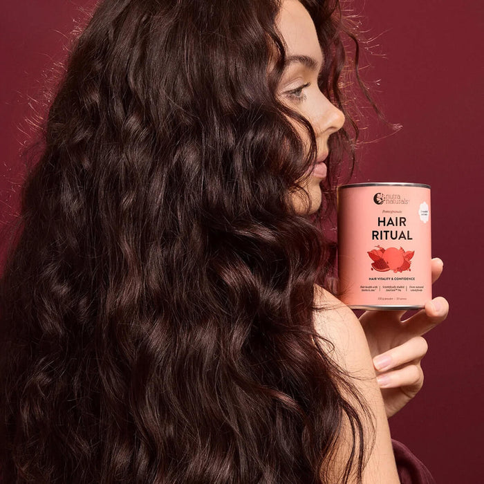 A woman with long, dark, wavy hair holds a pink tin labeled 'Hair Ritual' against a deep burgundy background.