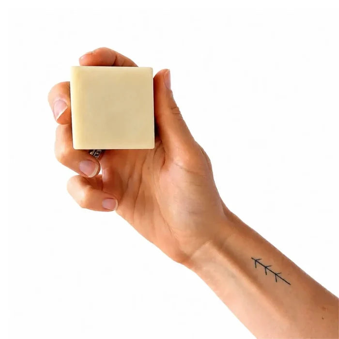 Hand holding a square bar of soap against a white background.