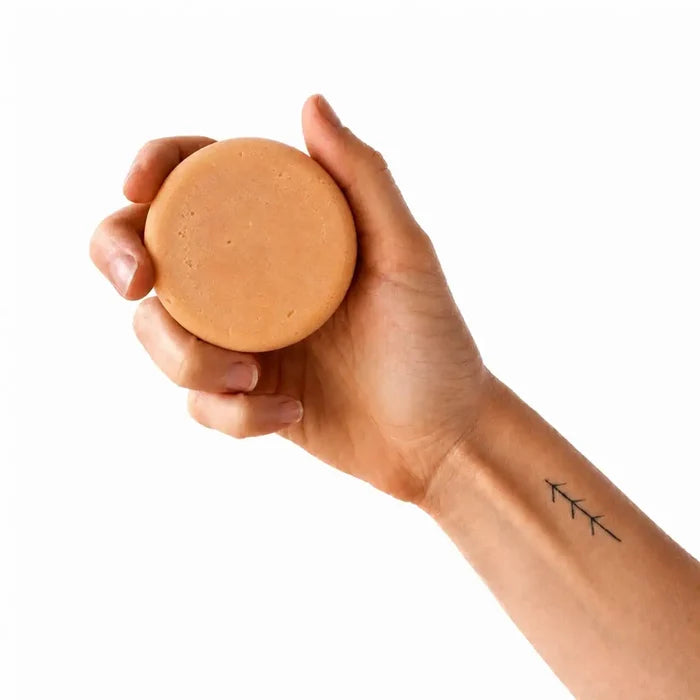 Hand holding a round, orange bar of soap against a white background.