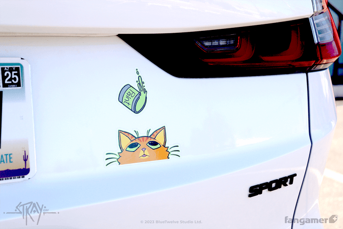 Stray stickers photographed on the back of a white car. The large sticker of the cat's face appears to be looking up at the falling paint sticker.