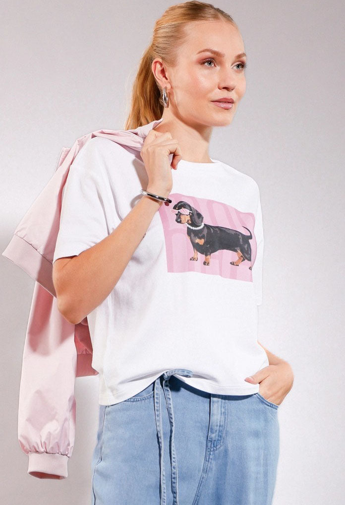 Woman wearing a white t-shirt with a dachshund graphic and a pink jacket on a gray background