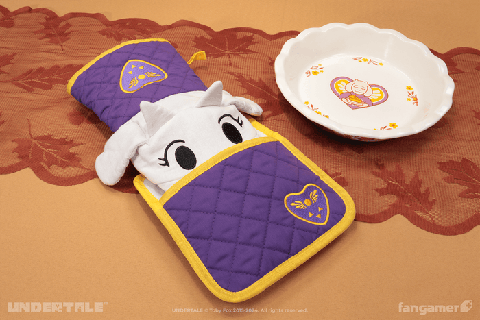 A photo of the Toriel oven mitt with its nose tucked into the included potholder. The Toriel's Kitchen pie dish is visible in the background.