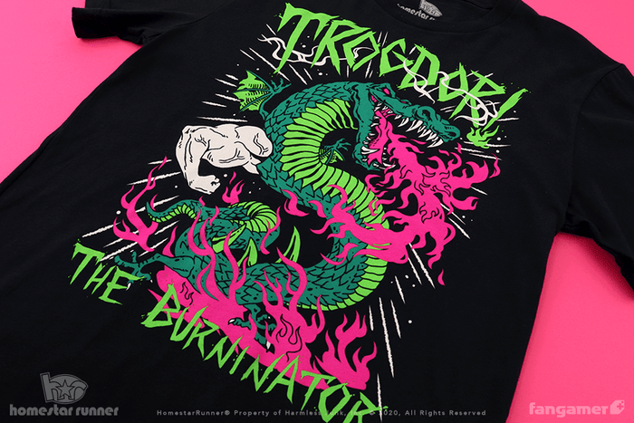 A photo of the Trogdor the Burninator shirt by Nina Matsumoto. It's a metal-style black shirt with Trogdor the Burninator written in jagged green text. A detailed drawing of Trogdor is covered in fuchsia flames.